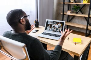 Das Bild zeigt einen Menschen vor einem Laptop mit Zoom-Meeting