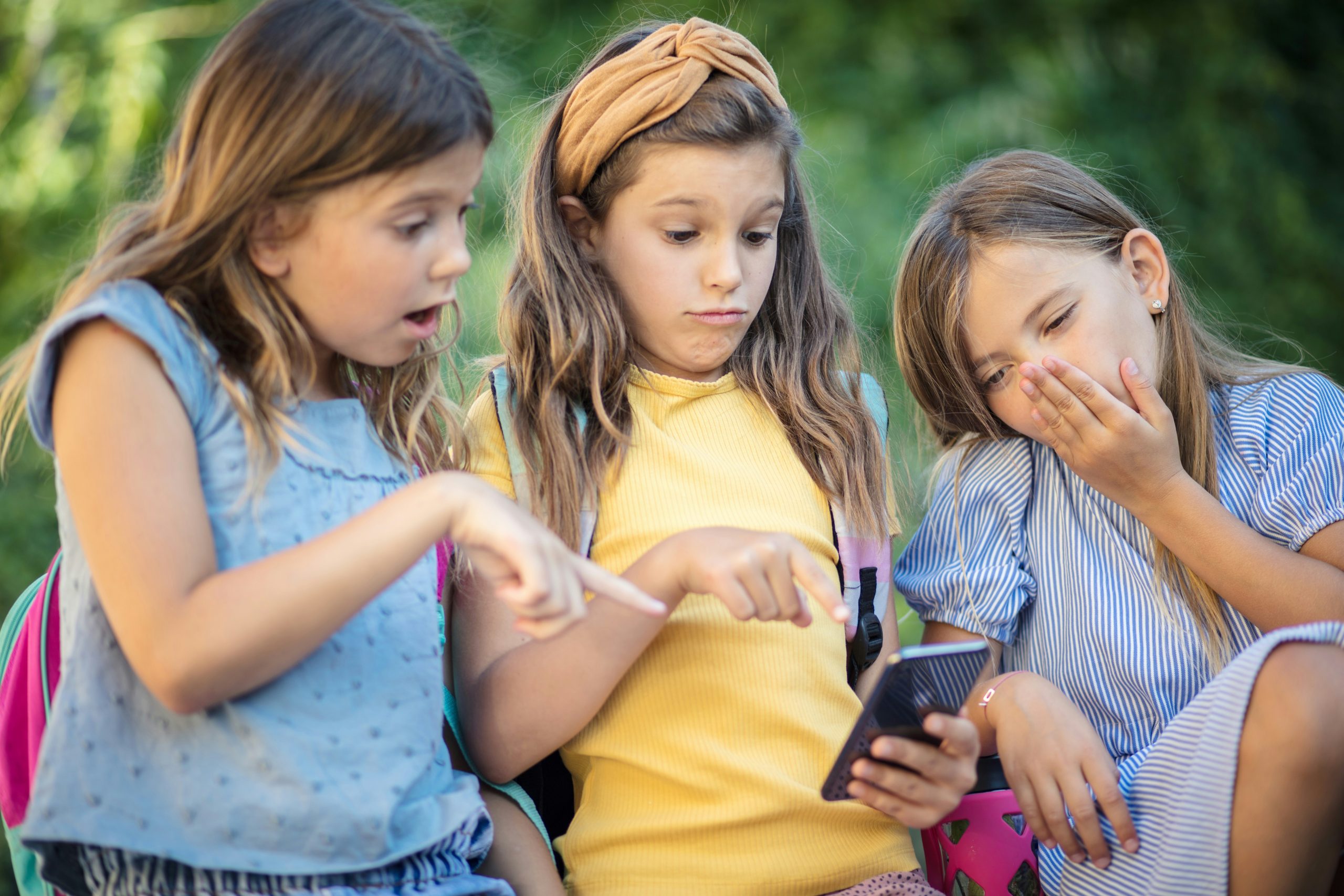 Das Bild zeigt drei Kinder, die auf ein Smartphone gucken